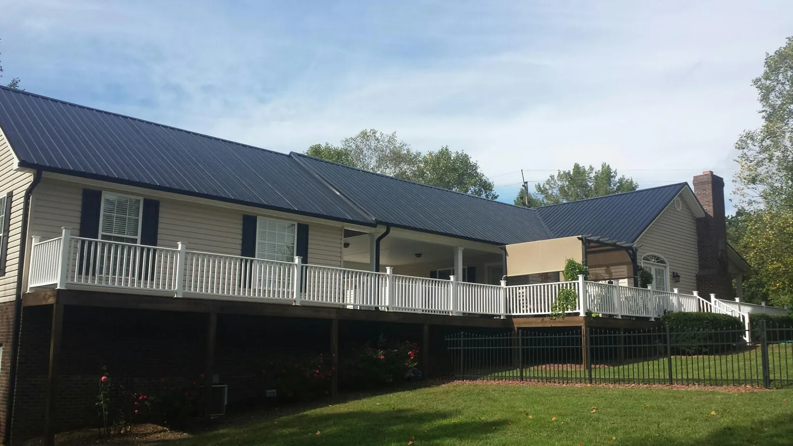 Black metal roof above a long white railed deck on a hillside home in Jersey City
